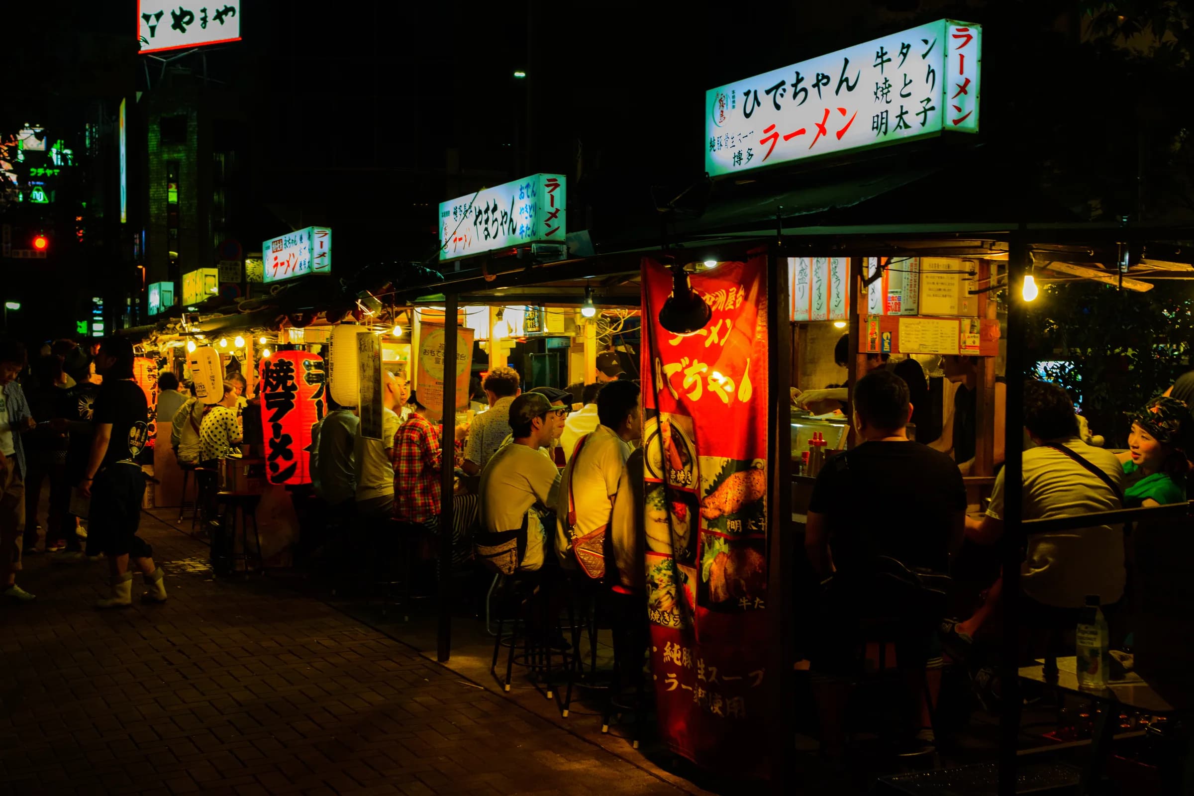 Nakasu yatai at night — lantern-lit food stalls along the river in Fukuoka with customers on stools under the awnings